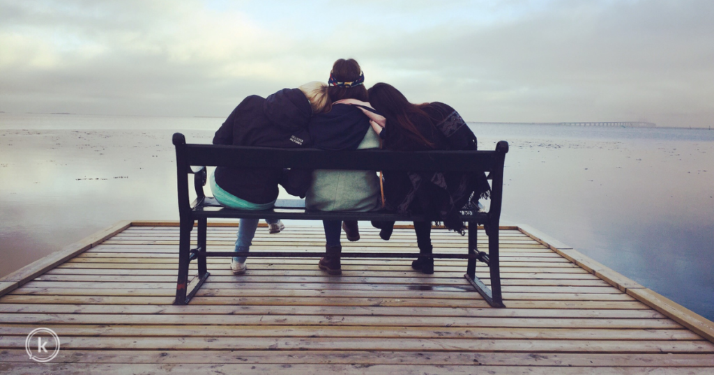 Three women sitting on a bench on a dock.